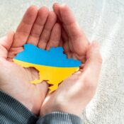 Hands holding national flag of Ukraine in the shape of the borders of Ukraine. Support for Ukraine