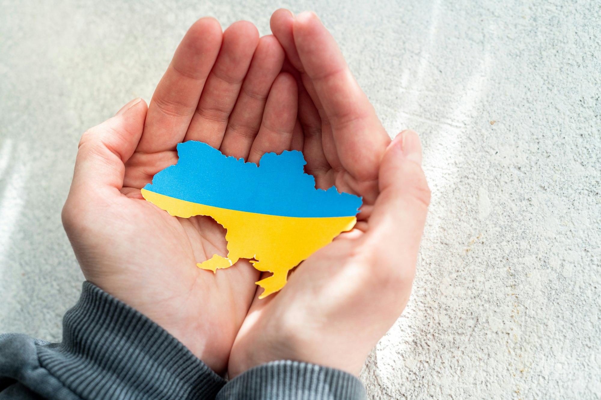 Hands holding national flag of Ukraine in the shape of the borders of Ukraine. Support for Ukraine